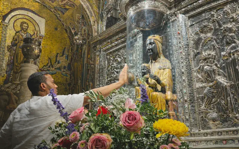 Black Madonna statue inside Montserrat basilica shrine with visitors approaching respectfully